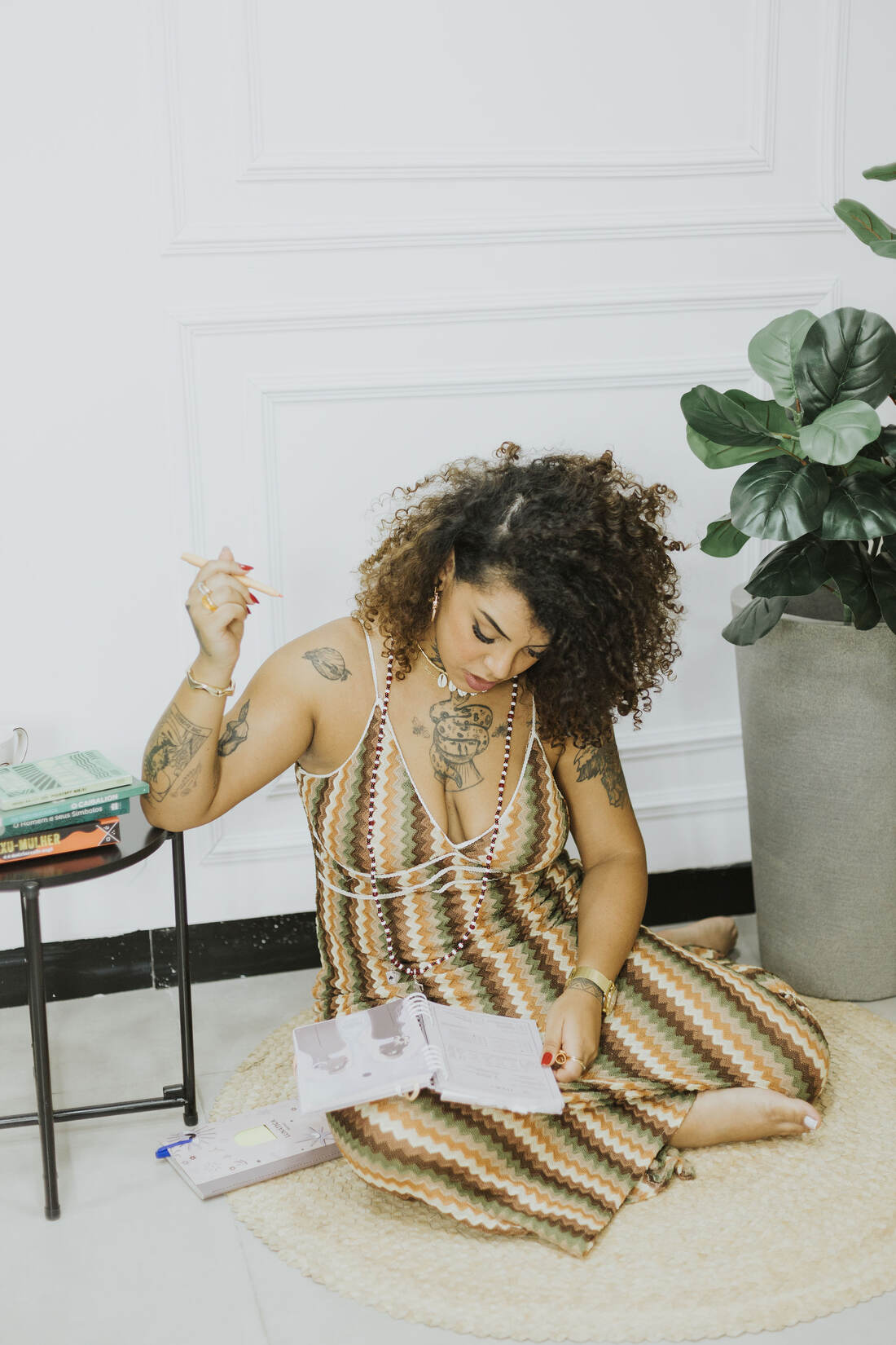 Solar sentada no chão, escrevendo em um caderno de estudos, cercada de livros